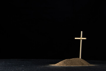 front view of little grave from sand with stick cross on dark floor death funeral israel