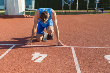 Front view of a Caucasian male sprinter in a race starting position, hands on the line and legs on...