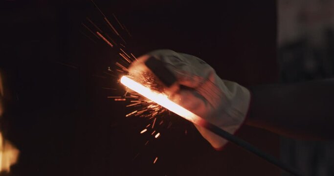 Spark, workshop and blacksmith with metal rod for sharpening, forging and welding by fire furnace. Factory, foundry and closeup of male worker for manufacturing, metalwork and industrial production