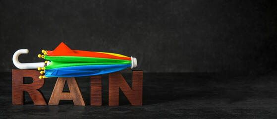 Mini umbrella and word RAIN on black background with space for text