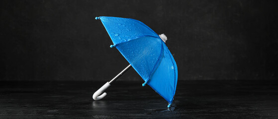 Mini blue umbrella with water drops on black background