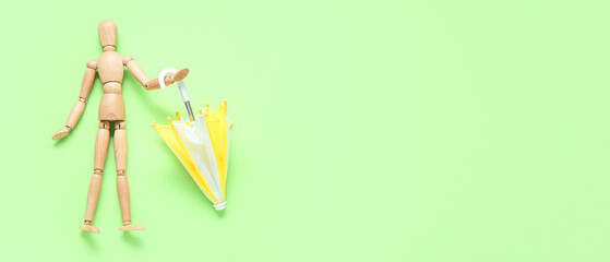 Wooden human figurine and mini umbrella on green background with space for text