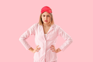 Upset young woman in pajamas on pink background