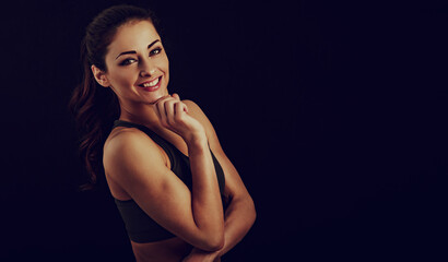 Obraz na płótnie Canvas Confident sport woman in sport bra smiling and looking in camera, fitness trainer standing front view, workout in gym on studio black background with empty copy space. Closeup