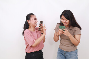 Two exciting asian woman standing while holding cell phone. Isolated on white