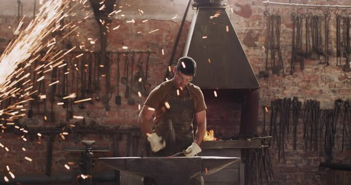 Blacksmith, fire and man with hammer on anvil in workshop for forging iron, steel or metal. Manufacturing, forge sparks and worker with equipment for industrial production of tools in small business.