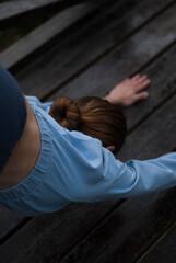 View on a girl with athletic body in blue gym suit is doing exercises in cloudy rainy weather.