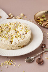 Plate of tasty Tahini halva with pistachios on beige background, closeup