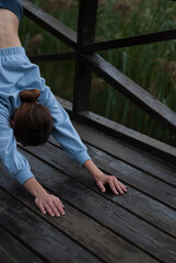 Girl with athletic body in blue gym suit is doing yoga exercises in cloudy rainy weather.