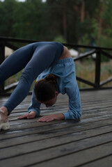 View on a girl with athletic body in blue gym suit is doing yoga in cloudy rainy weather in the park.