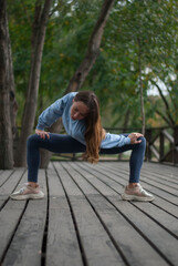 View on young girl with athletic body is doing acrobatics exercises in cloudy weather in the park