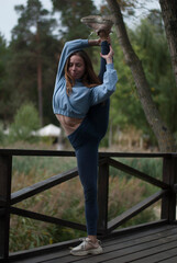 Young girl in blue gym suit is doing acrobatics exercises in the park in cloudy weather