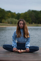 Fototapeta na wymiar View on young girl is doing yoga near lake