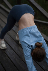 View on a girl with athletic body is doing exercises in the park in cloudy rainy weather.