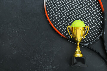 Gold cup with ball and tennis racket on dark background