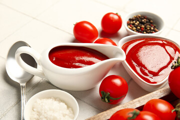 Gravy boat and bowl of tasty ketchup with fresh tomatoes on white tile background
