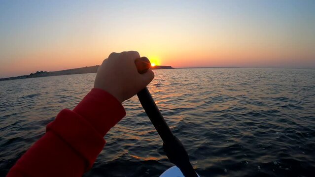 Woman floating on SUP board in the sea at sunset dawn on a summer morning. Person floating on a white SUP board and paddles on the water during sunrise sunset. POV. Seascape sea landscape background