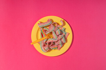 Rainbow sour belts in a yellow plate, on bright pink background. Food concept, excessive sugar...
