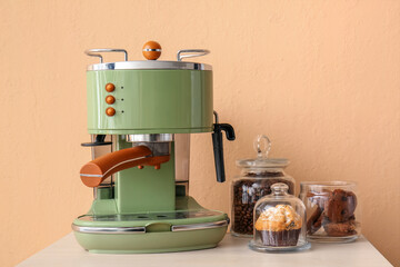 Table with coffee machine, snacks and cups near beige wall