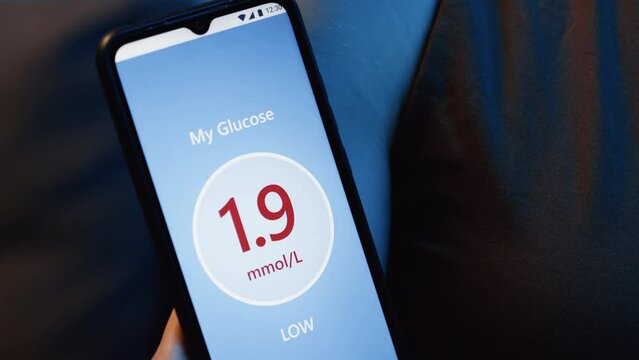 Extreme close up of mobile app showing low glucose level in smartphone held by unrecognizable woman with patch on shoulder