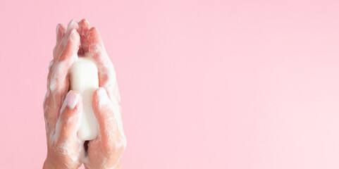 Washing of hands with soap. Cleaning hands. Closeup on woman hands with soap bar on pastel pink background.