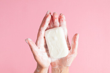 Washing of hands with soap. Cleaning hands. Closeup on woman hands with soap bar on pastel pink...