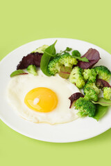Plate with tasty fried egg, broccoli and spinach on green background