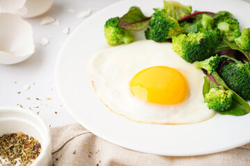 Plate with tasty fried egg, broccoli and spinach on light background