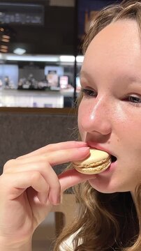 Teenage girl brown-haired woman with a mole above her lip eats makarun close-up slowly biting it off and blows with pleasure. vertical video