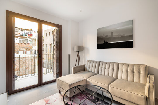 Cozy living room with a corner sofa, a table and a lamp with a picture on the background of a panoramic window with a balcony overlooking the courtyard of the house