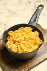 Pot with raw conchiglie pasta on grunge background