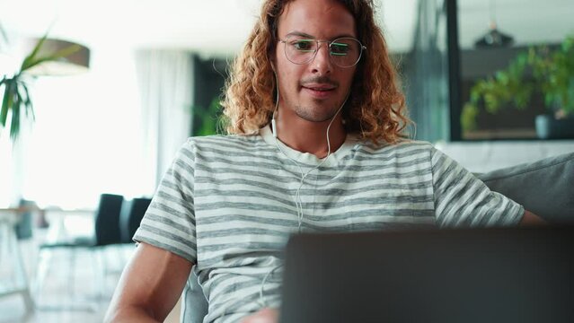 Cute curly long haired man in eyeglasses working on laptop in office  