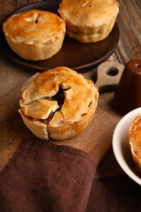 Wooden board with tasty meat pot pies on table