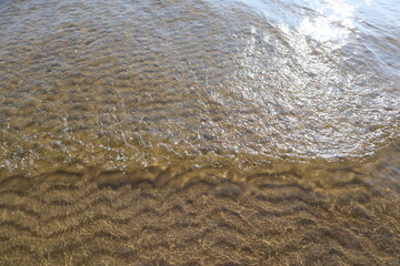 Beautiful background with transparent water and ripples on sandy bottom. Sea waves and gritty surface texture created a pattern of dunes on sand of seabed.