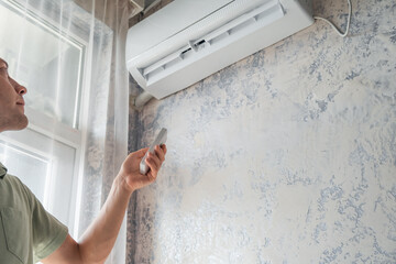 Young woman switching on air conditioner at home for comfort temperature with remote controller in...