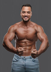 Fototapeta na wymiar Incredibly attractive male model with a well-toned physique flashes a bright smile as he poses shirtless against a simple grey background, exuding charisma and magnetism