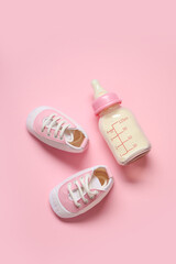Bottle of milk for baby with booties on pale pink background