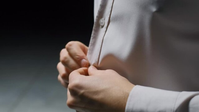 A man in a white shirt fastens the buttons in a dark room. Stock footage. Businessman getting dressed.
