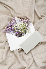 Envelope with beautiful gypsophila flowers and blank invitation card on grey crumpled tablecloth