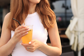 Passion fruit lemonade. Summer drink in the hands of a girl. Takeaway lemonade. Cold lemonade with ice in a female hand against a summer street cafe