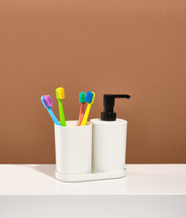 Four multicolored toothbrushes stand in a glass. Dispenser with liquid soap. Cleaning the teeth.