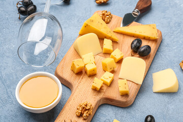 Wooden board with pieces of tasty cheese, wine glass and honey on grey background