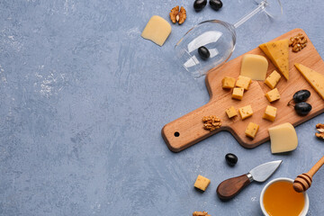 Wooden board with pieces of tasty cheese, wine glass and honey on grey background