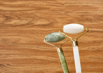 Green and white roller cosmetic facial massagers on a wooden background. Skin care ingredients and accessories. Copy space for text.