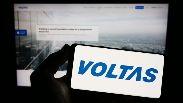 Stuttgart, Germany - 06-16-2023: Person holding smartphone with logo of Indian home appliances company Voltas Limited on screen in front of website. Focus on phone display.