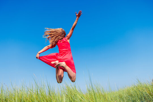 Woman with red dress and long hair jump in blue sky- active, wellness, freedom concept