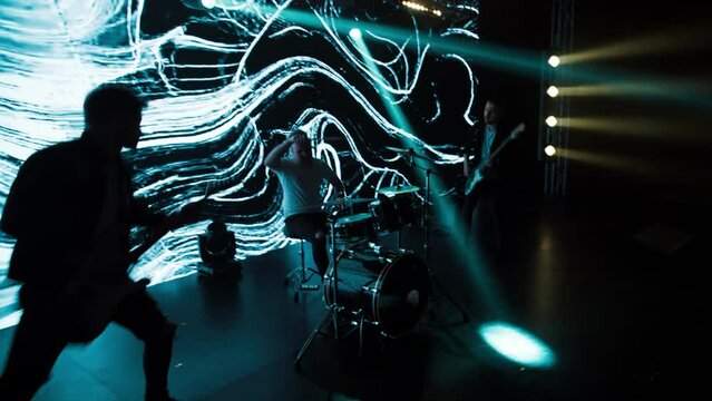 Jib shot of a drummer performing his solo during rock band concert on stage of a large venue, surrounded by bright flashing stage lights