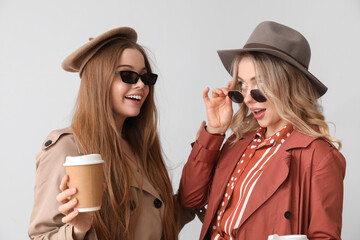 Young sisters with cups of coffee on light background