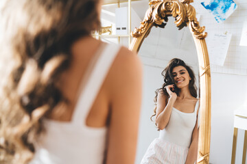 Naklejka premium Happy young lady in sleepwear looking in mirror at home