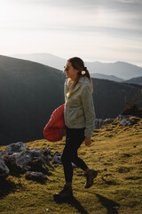 Girl with long hair, sunglasses and mountain clothes walks on the mountain at sunset while smiling.